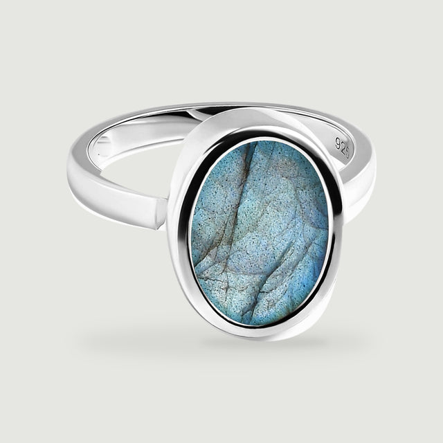 A polished sterling silver ring with an oval blue labradorite rests on a light grey surface.