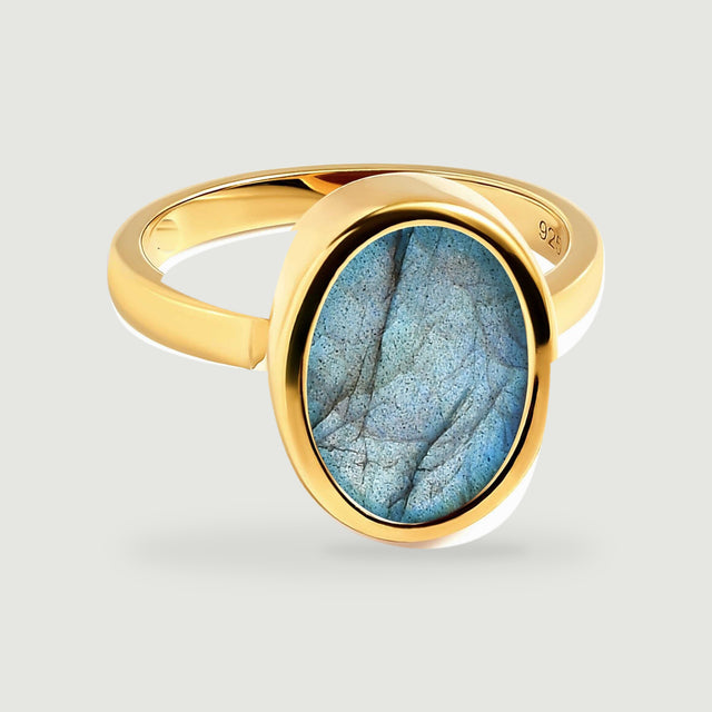 An oval blue labradorite is framed by a polished yellow gold vermeil ring on light grey.