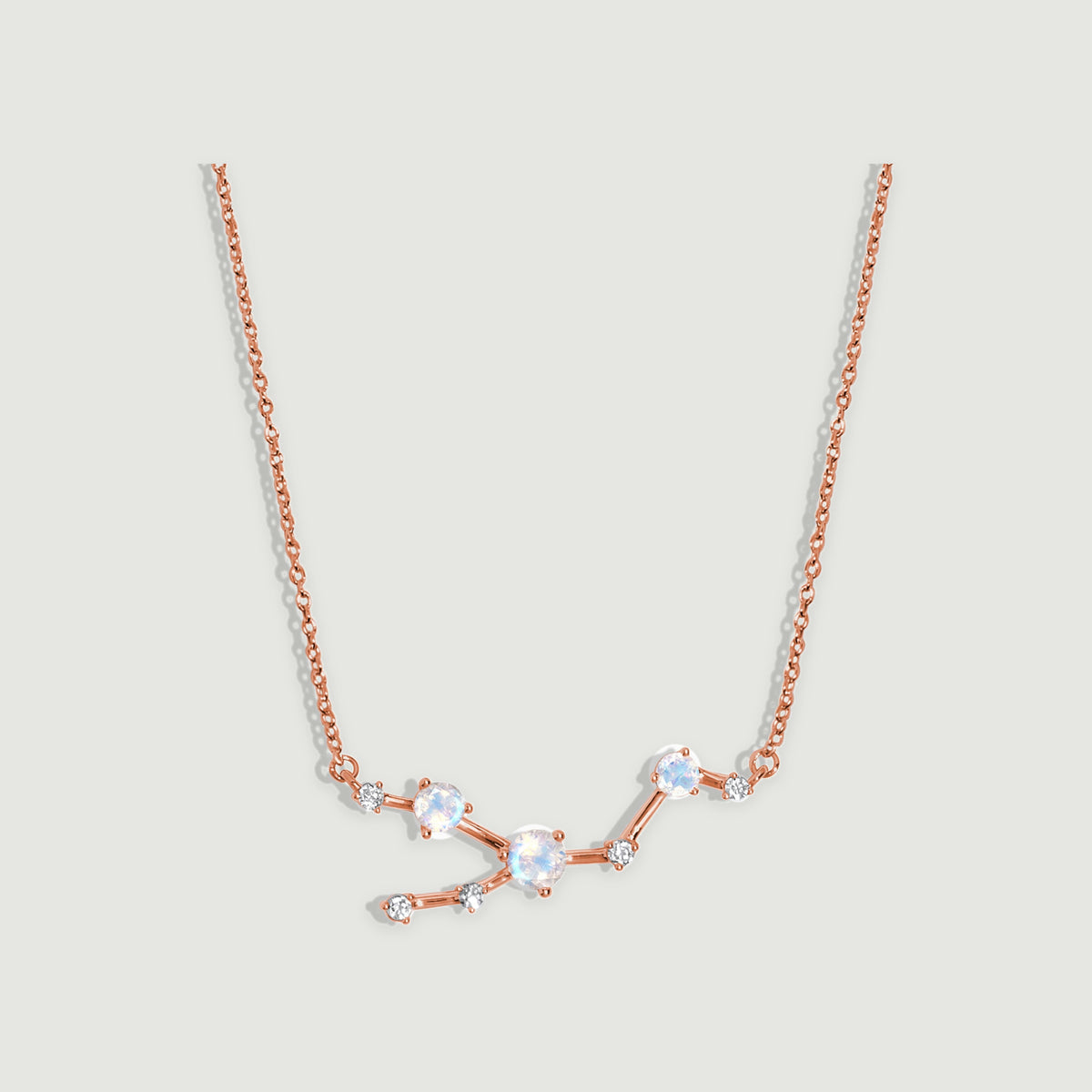 A rose gold chain frames a branching centerpiece with pale blue faceted moonstones on a light grey surface.