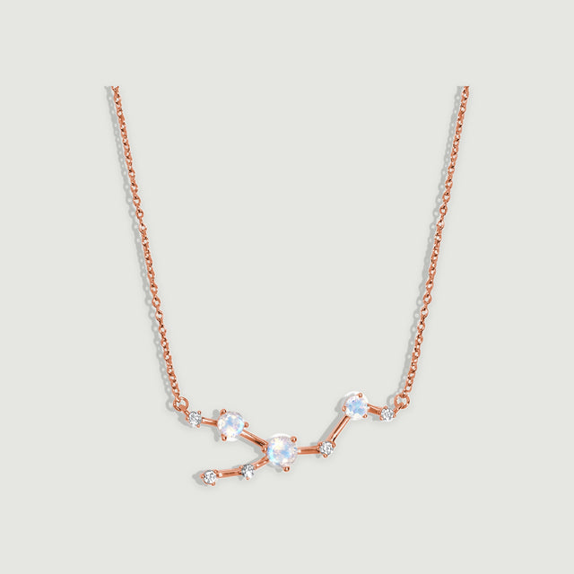 A rose gold chain frames a branching centerpiece with pale blue faceted moonstones on a light grey surface.