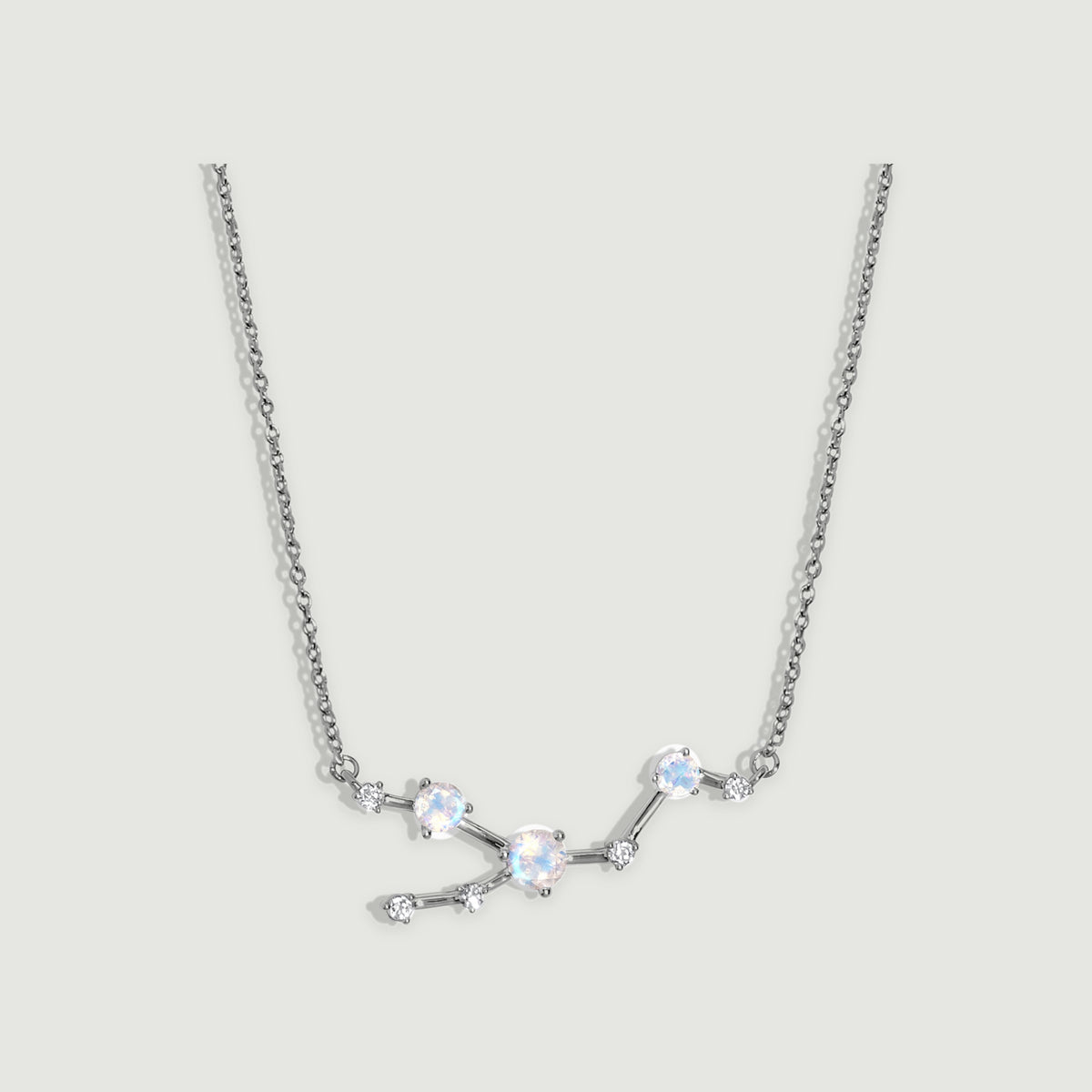 A silver necklace has polished connecting bars and round prong-set stones against a softly shaded grey background.