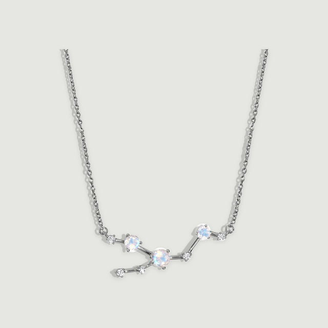A silver necklace has polished connecting bars and round prong-set stones against a softly shaded grey background.