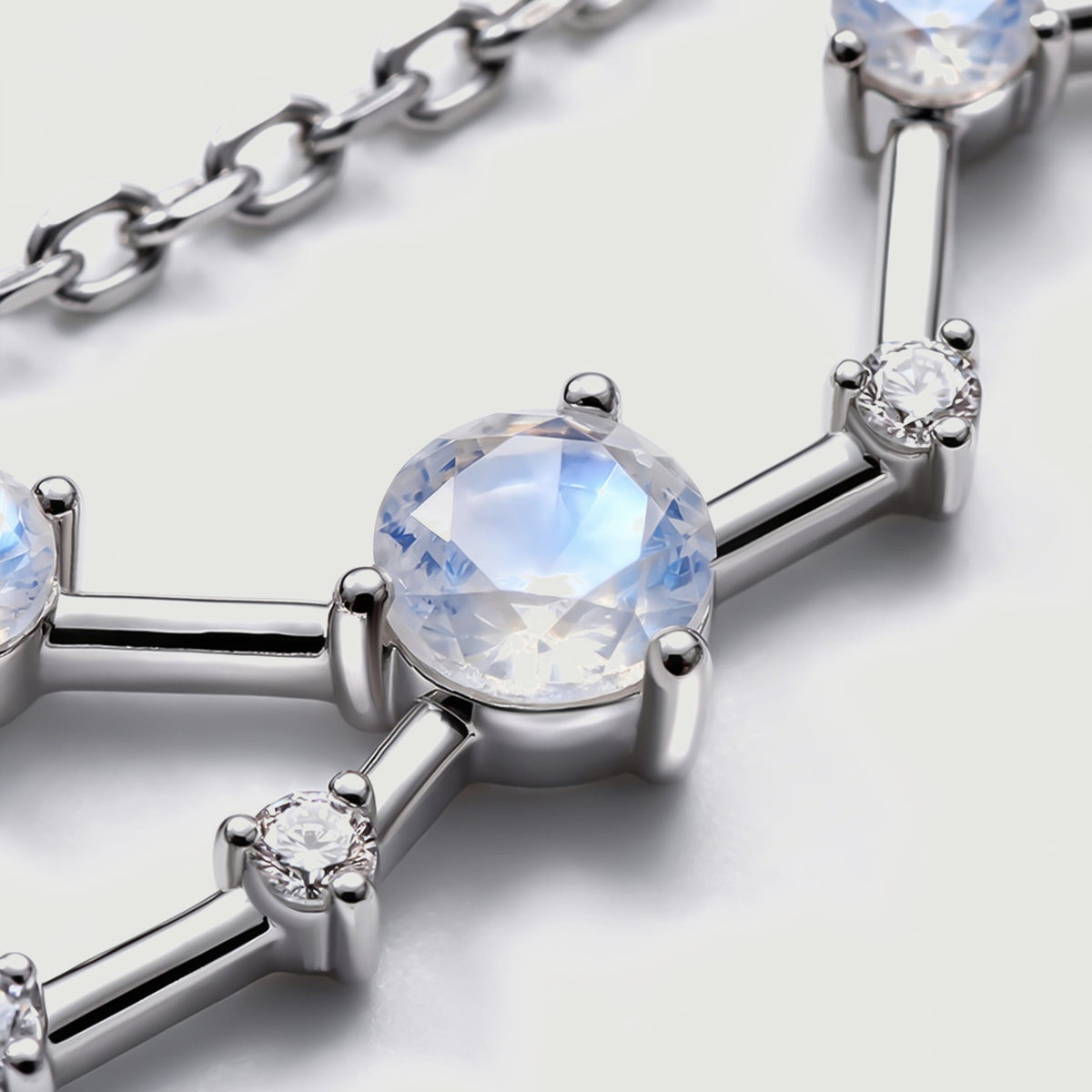 A large round moonstone sits in a polished silver setting with a small clear stone and chain links nearby.