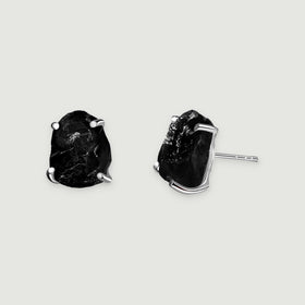 A pair of black obsidian studs displays silver prongs and a straight earring post on a pale gray background.