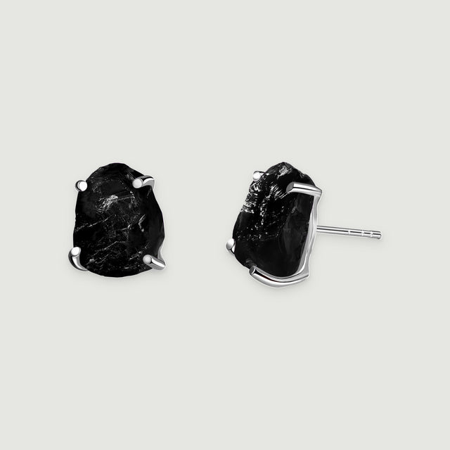A pair of black obsidian studs displays silver prongs and a straight earring post on a pale gray background.