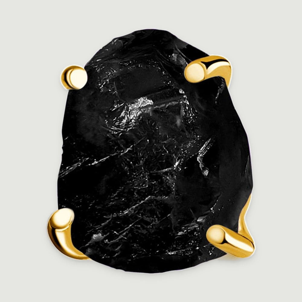 A close view reveals the uneven black obsidian surface held by four yellow gold prongs.