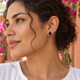 A woman with curly dark hair wears a rose gold black obsidian stud beside a terracotta wall and pink flowers.