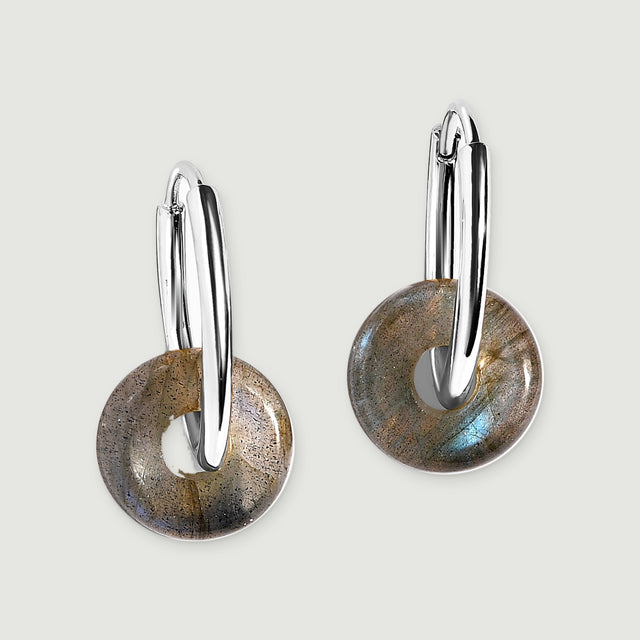Two silver-tone hoops with circular labradorite drops rest diagonally against a pale gray background.