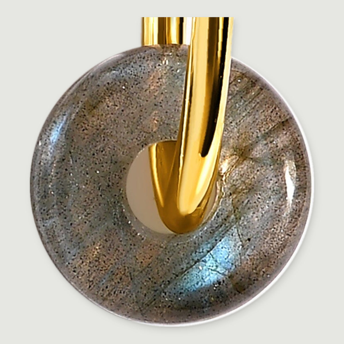 A close view shows blue flashes and dark speckles in a labradorite disc threaded onto a yellow gold hoop.