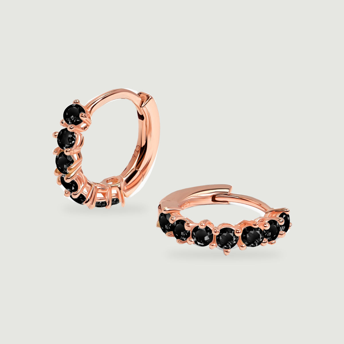 Two black onyx hoop earrings in rose gold vermeil are arranged upright and flat on a light gray surface.