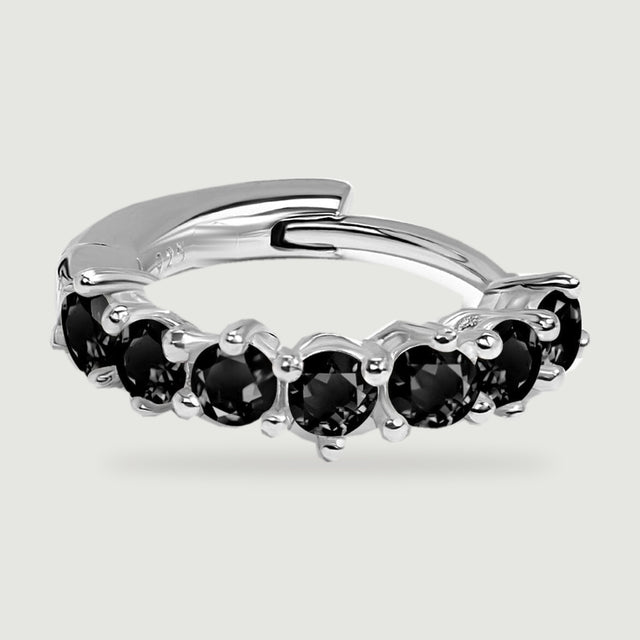 Round faceted black stones sit in silver prongs along the front of a flat hoop earring.