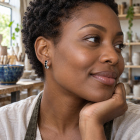 A woman with short coily hair wears a silver black onyx hoop earring in a pottery studio.