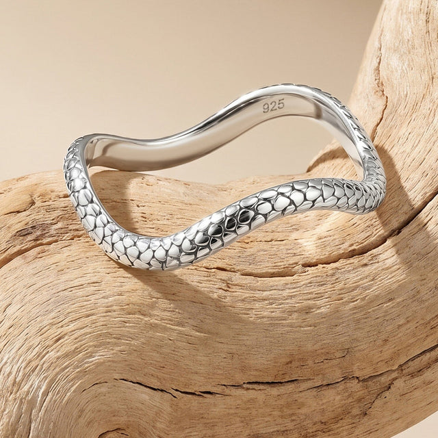 An angled silver ring rests on clean pale wood with its curving outline and smooth interior visible.