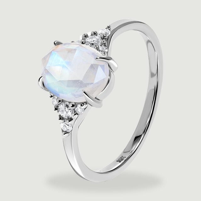 The tilted white gold ring reveals curved prongs, faceted moonstone, and diamonds along both shoulders.