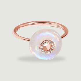 A rose gold ring with a polished slender band and an iridescent moonstone disc on a light gray background.