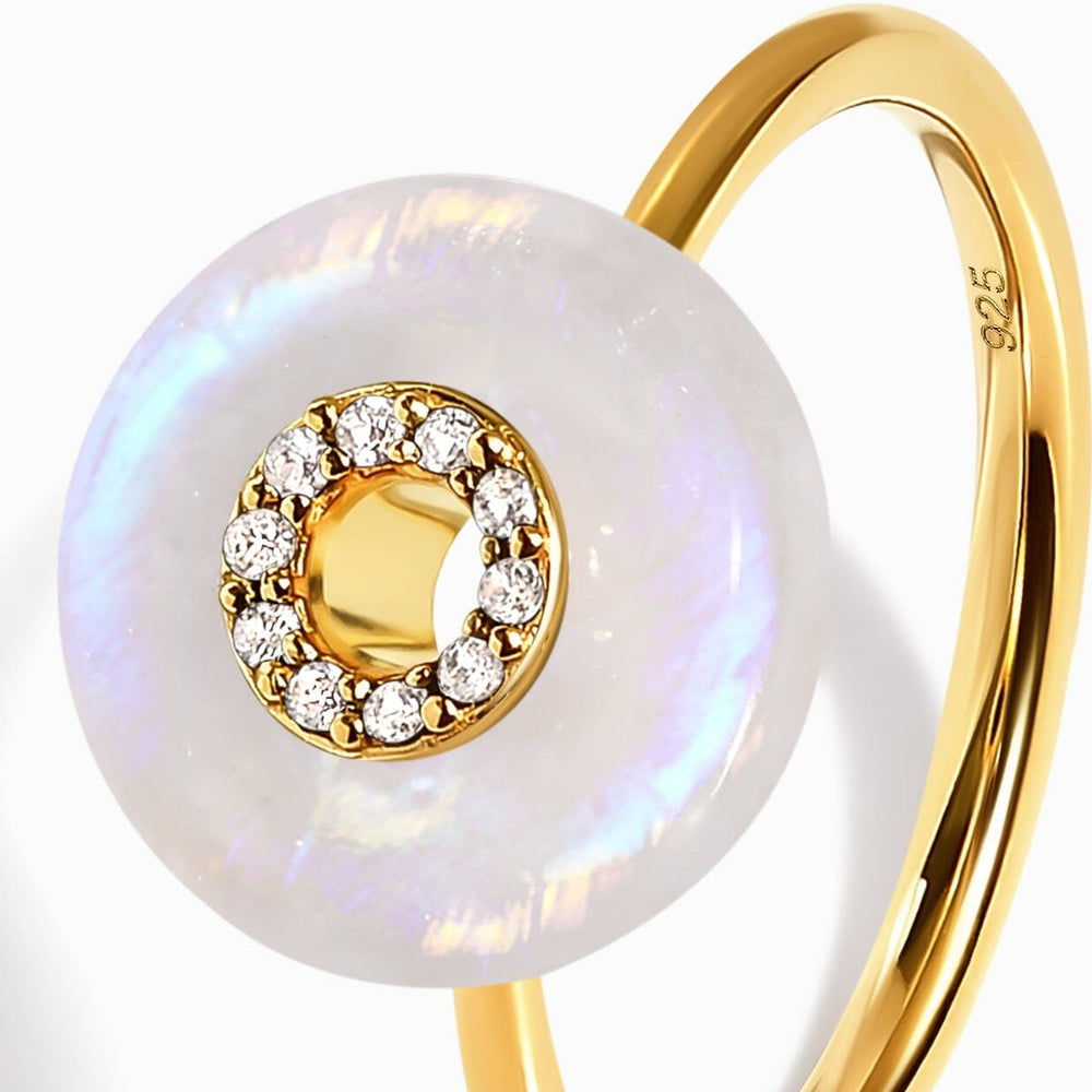 A close view of the moonstone disc and clear stone setting beside a curved yellow gold band.