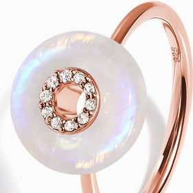 A translucent moonstone disc reflects blue and pink light beside the curved rose gold ring shank.