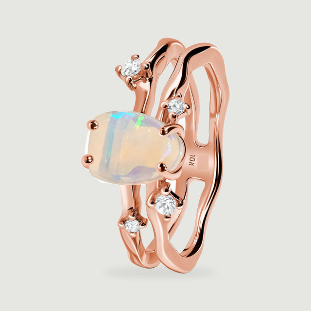 The upright rose gold ring shows its raised opal setting and open double band from an oblique angle.