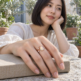 A woman wears the rose gold opal ring with her hand resting on a linen-covered book in a leafy courtyard.