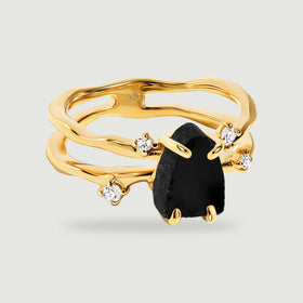 A yellow gold vermeil ring with raw black obsidian and four clear round stones rests on a light gray surface.
