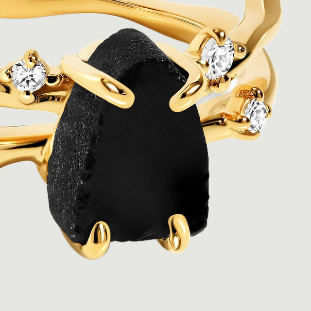 A close view shows the rough black obsidian surface held by yellow gold claws beside clear round stones.