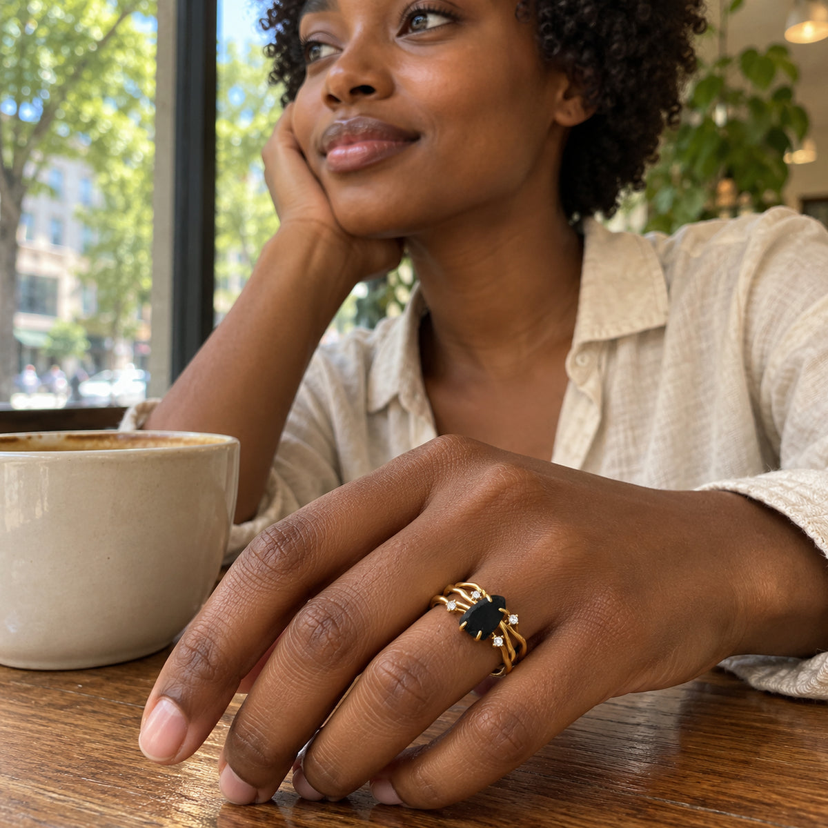 A woman wears the yellow gold vermeil black obsidian ring with her hand resting beside a ceramic cup on a wooden cafe table.