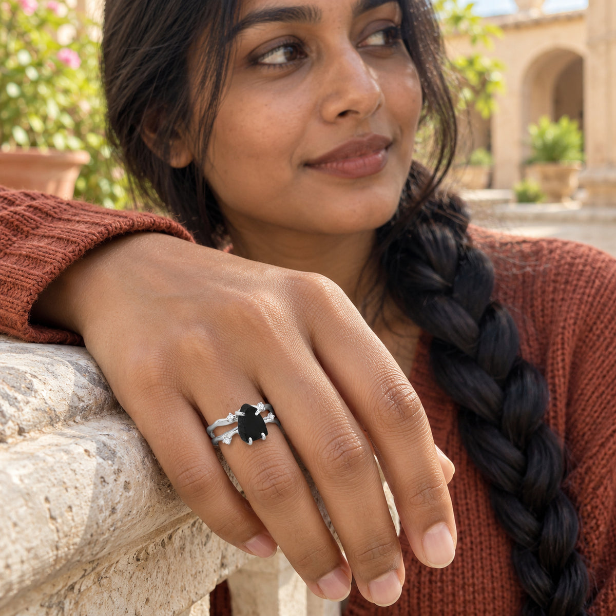 A woman wears the sterling silver black obsidian ring while resting her hand on a pale stone courtyard ledge.