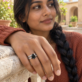 A woman wears the sterling silver black obsidian ring while resting her hand on a pale stone courtyard ledge.