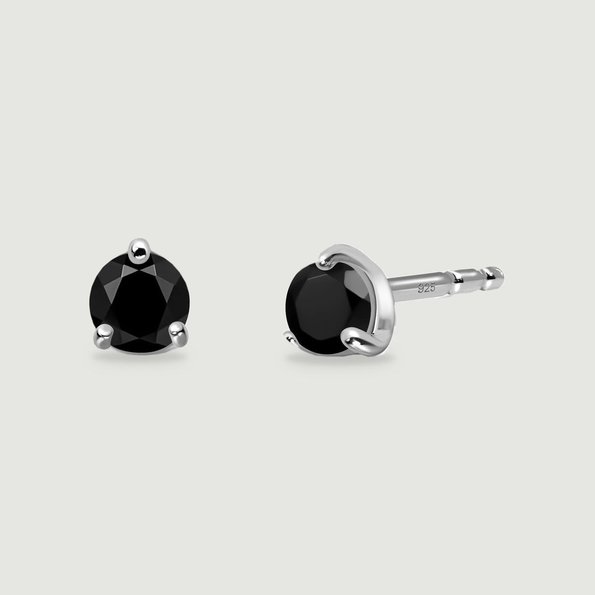 Two round faceted black obsidian studs show polished silver prongs and a straight earring post on a light gray surface.
