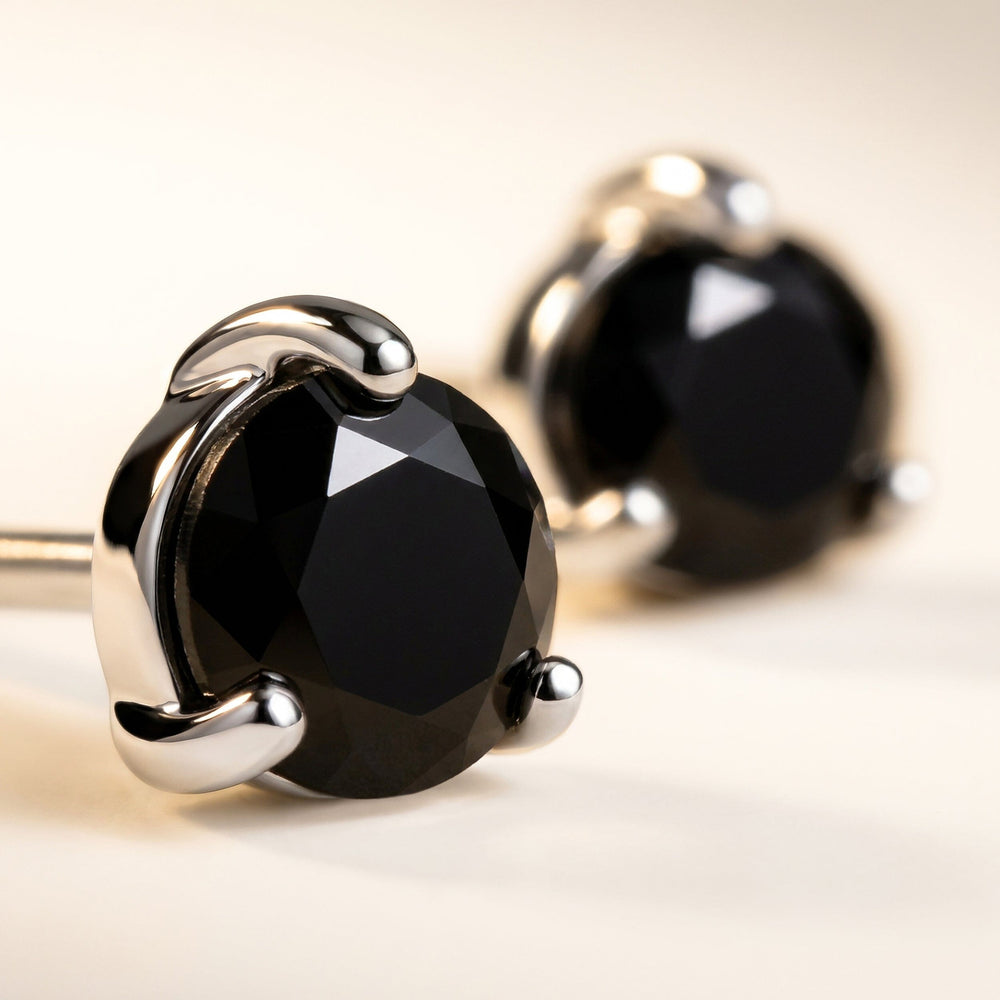 A close view shows a faceted black obsidian stone held by three rounded silver prongs, with its matching stud behind it.