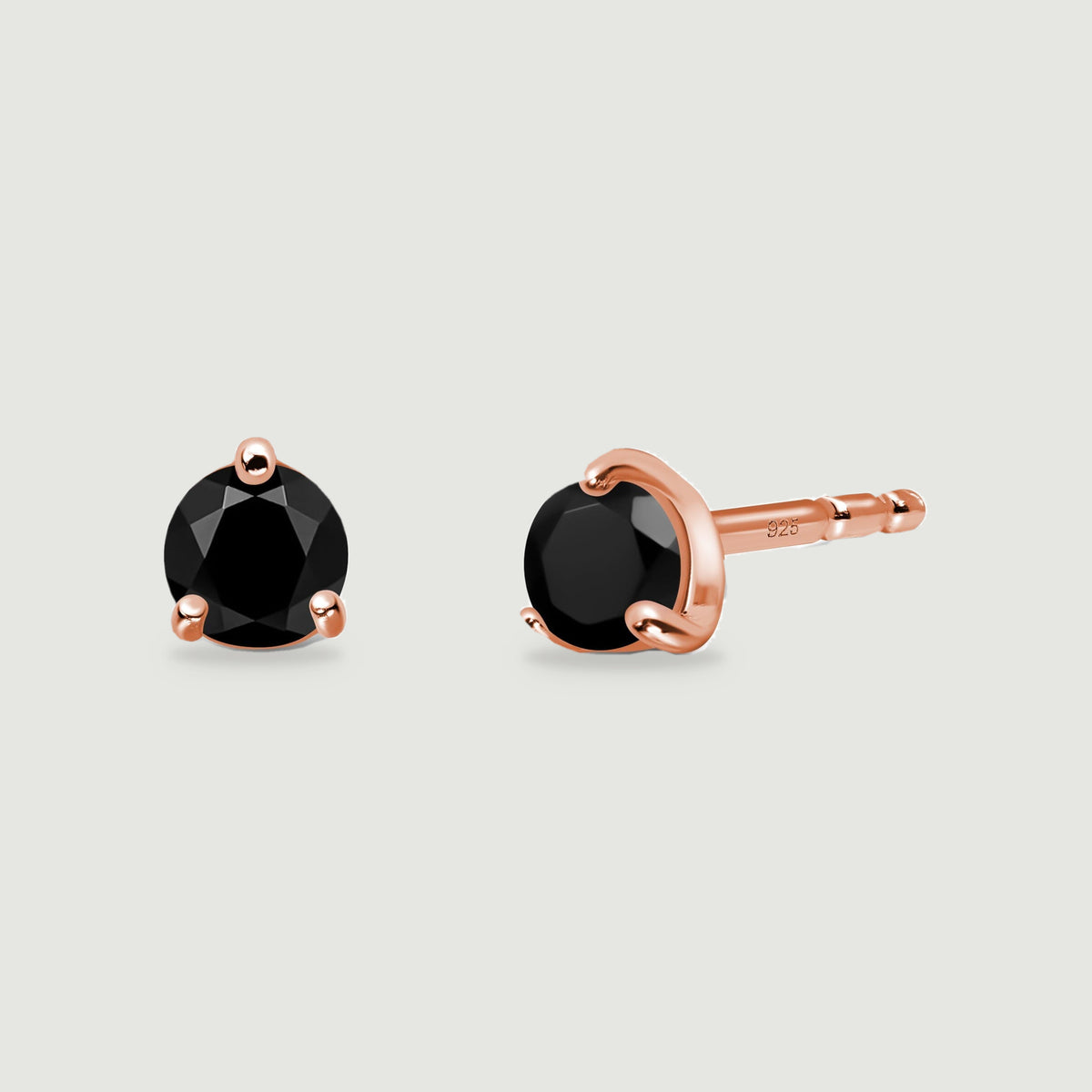 A pair of black obsidian stud earrings displays warm rose gold prongs and a visible post against light gray.