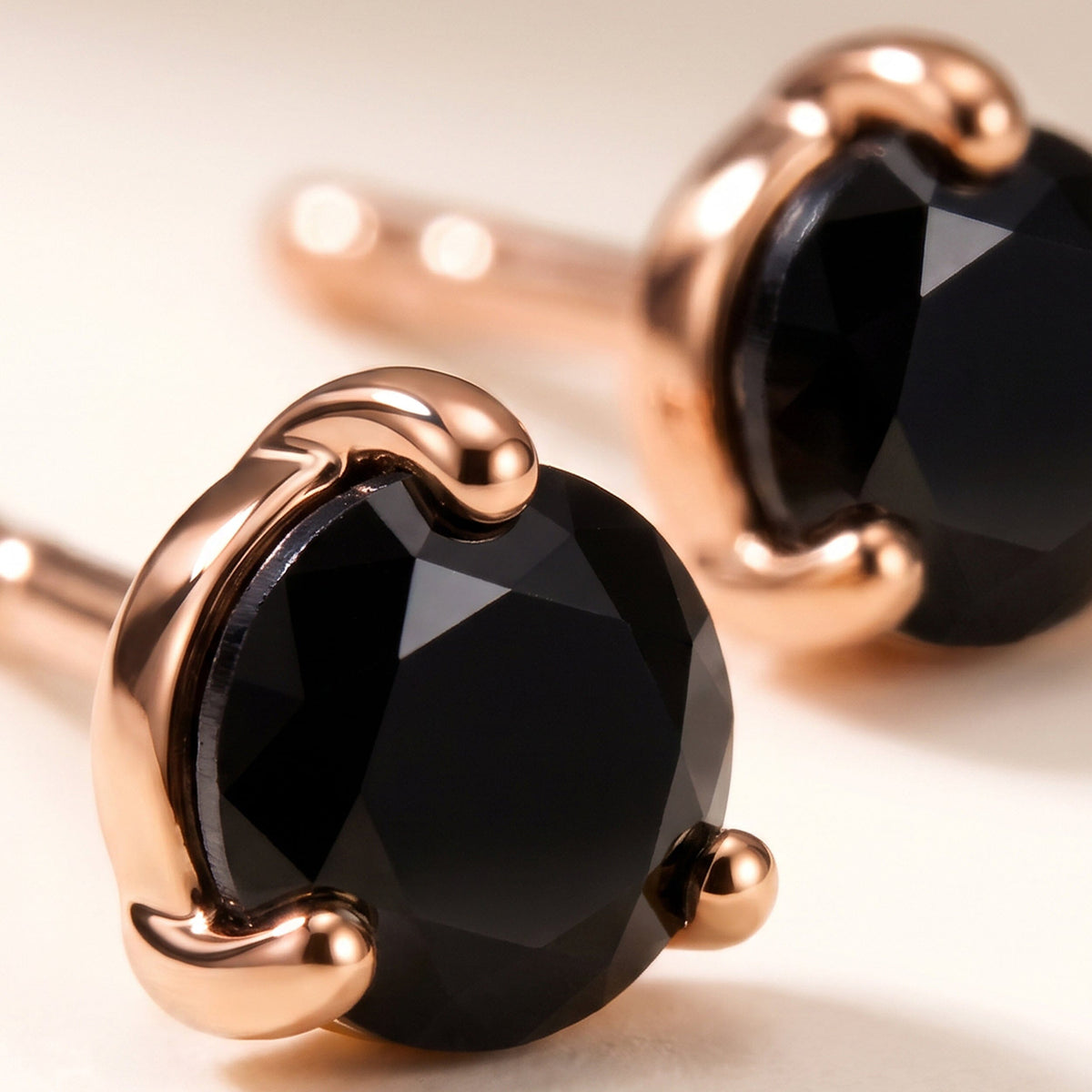 Rose gold prongs curve around a black faceted stone in the foreground, while the second stud rests softly out of focus.