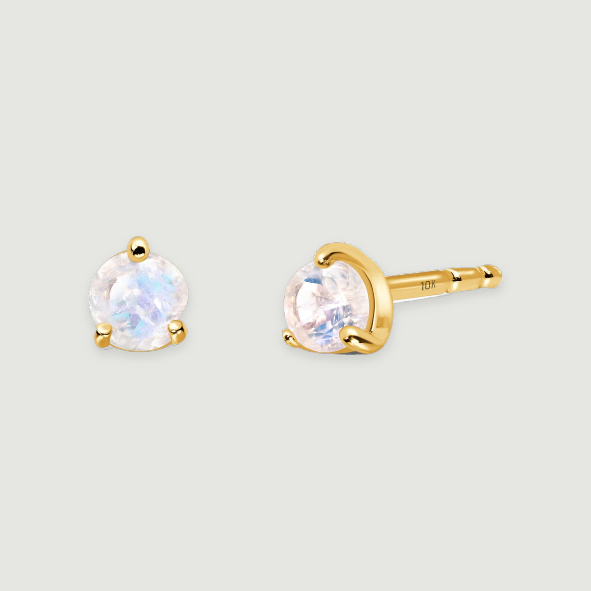 Two yellow gold moonstone earrings rest together, and a 10K stamp is visible on the exposed post.