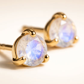 Yellow gold vermeil prongs surround a pale faceted moonstone on a cream tabletop, with the matching stud in the background.