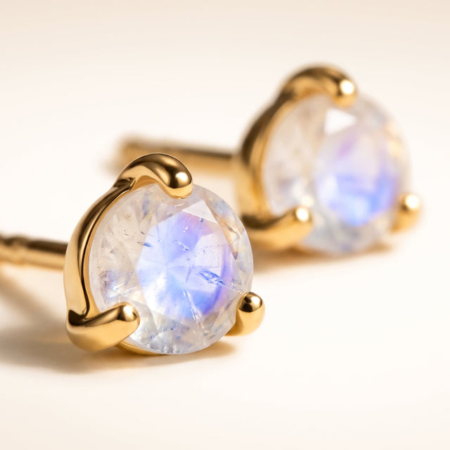 Yellow gold vermeil prongs surround a pale faceted moonstone on a cream tabletop, with the matching stud in the background.