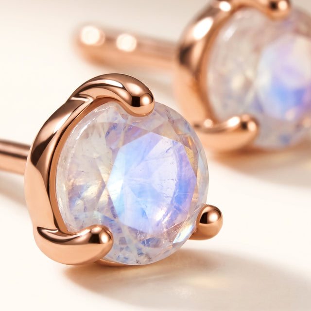 A rose gold vermeil moonstone stud fills the foreground, showing its rounded prongs and translucent blue-violet facets.