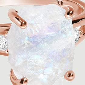 A close view shows the uneven white moonstone surface held by polished rose gold prongs.