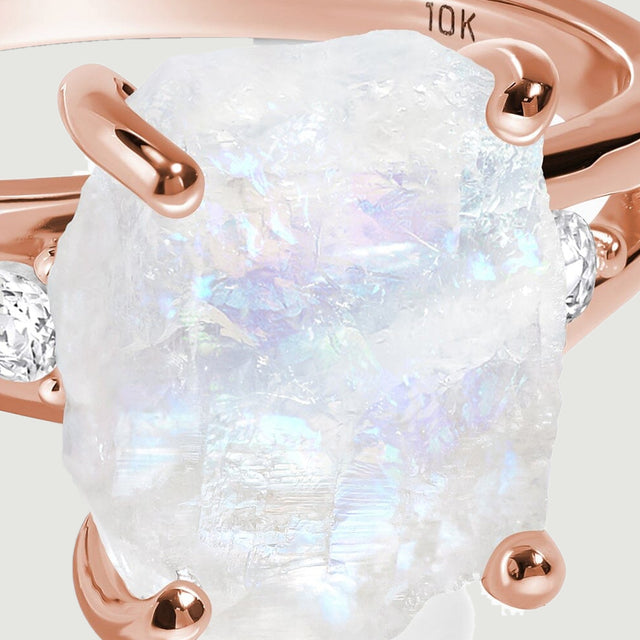 A close view shows the uneven white moonstone surface held by polished rose gold prongs.