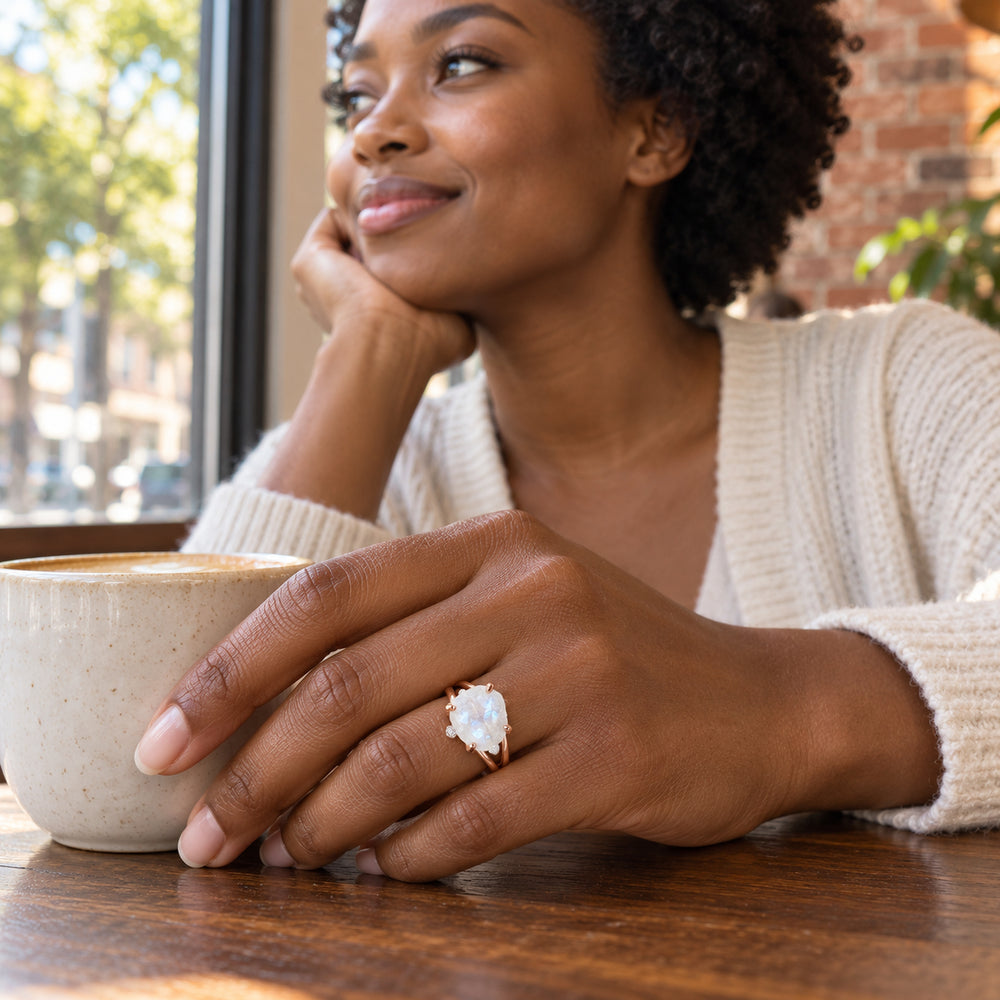 A woman wears the rose gold moonstone ring while resting her hand beside a ceramic coffee cup on a wooden cafe table.