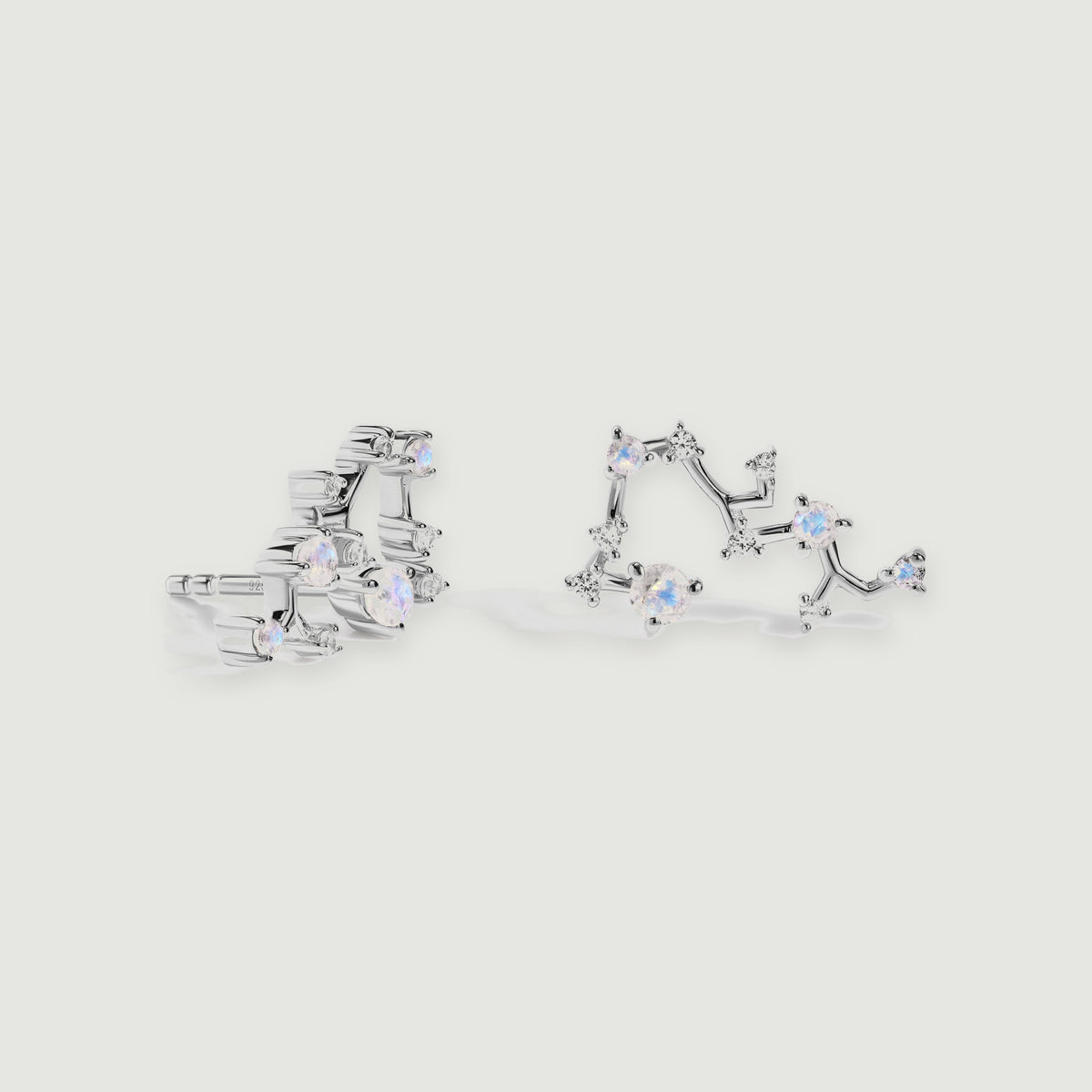 Silver constellation studs are arranged with one front view and one side view on a soft gray background.