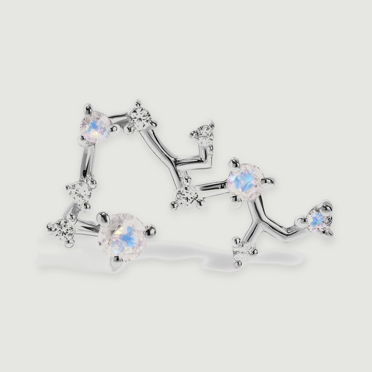 A silver stud is enlarged to show the polished constellation branches and individual round gemstone settings.