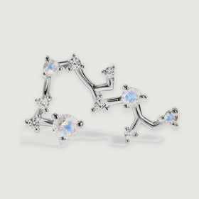 A silver stud is enlarged to show the polished constellation branches and individual round gemstone settings.