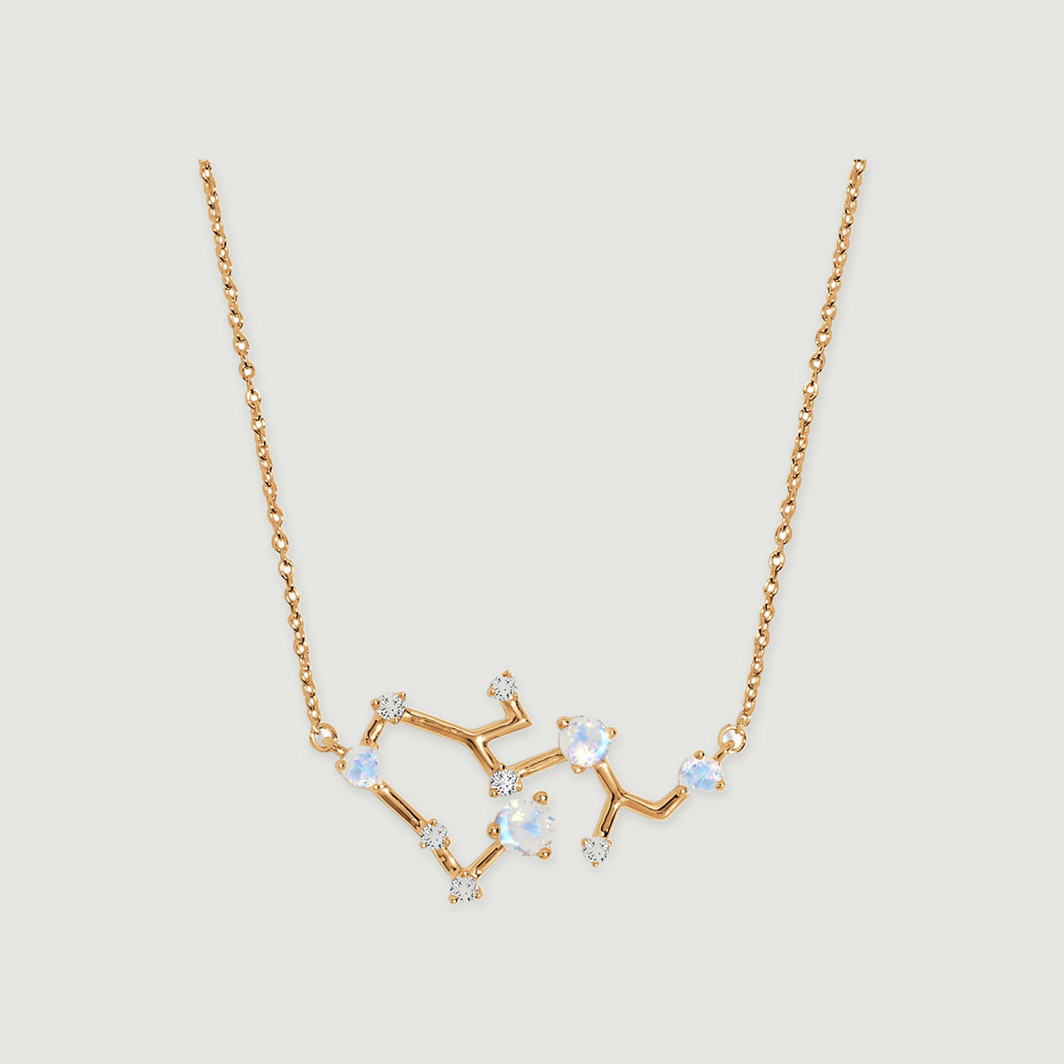 A yellow gold necklace with a branching pendant, round pale stones, and small clear accents is centered on a light gray background.