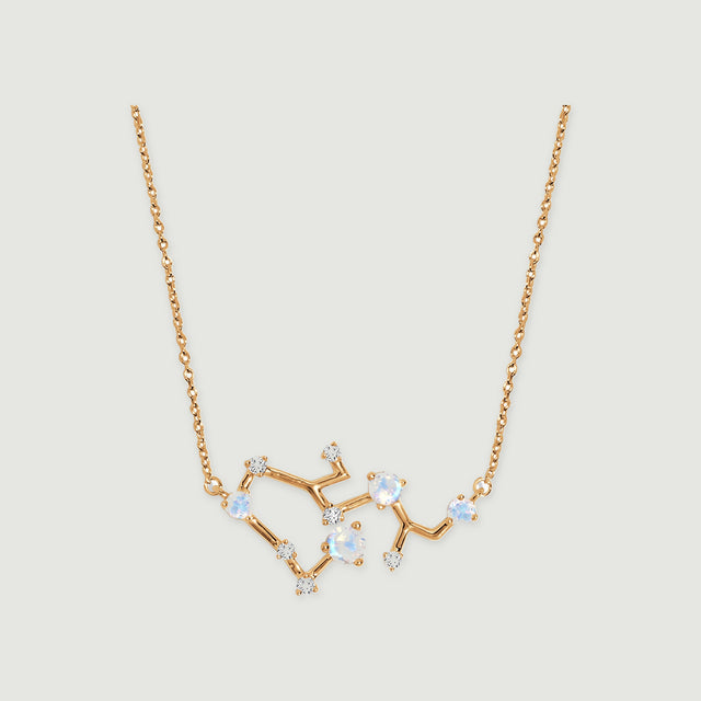 A yellow gold necklace with a branching pendant, round pale stones, and small clear accents is centered on a light gray background.