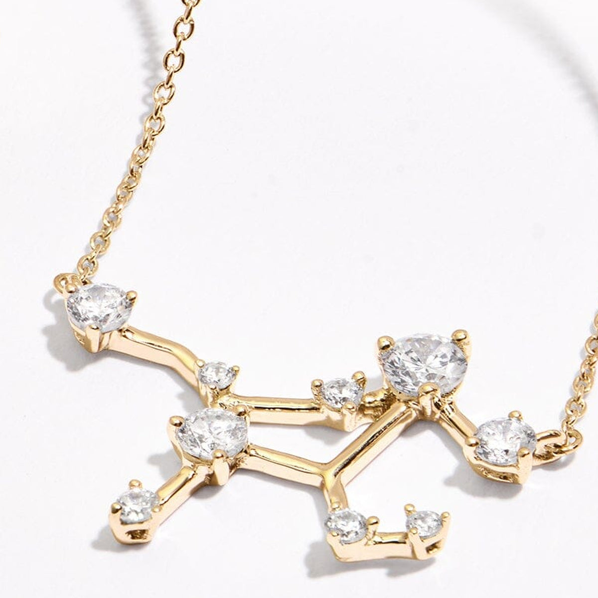 A yellow gold constellation pendant and portions of its chain lie on a pale tabletop in angled light.