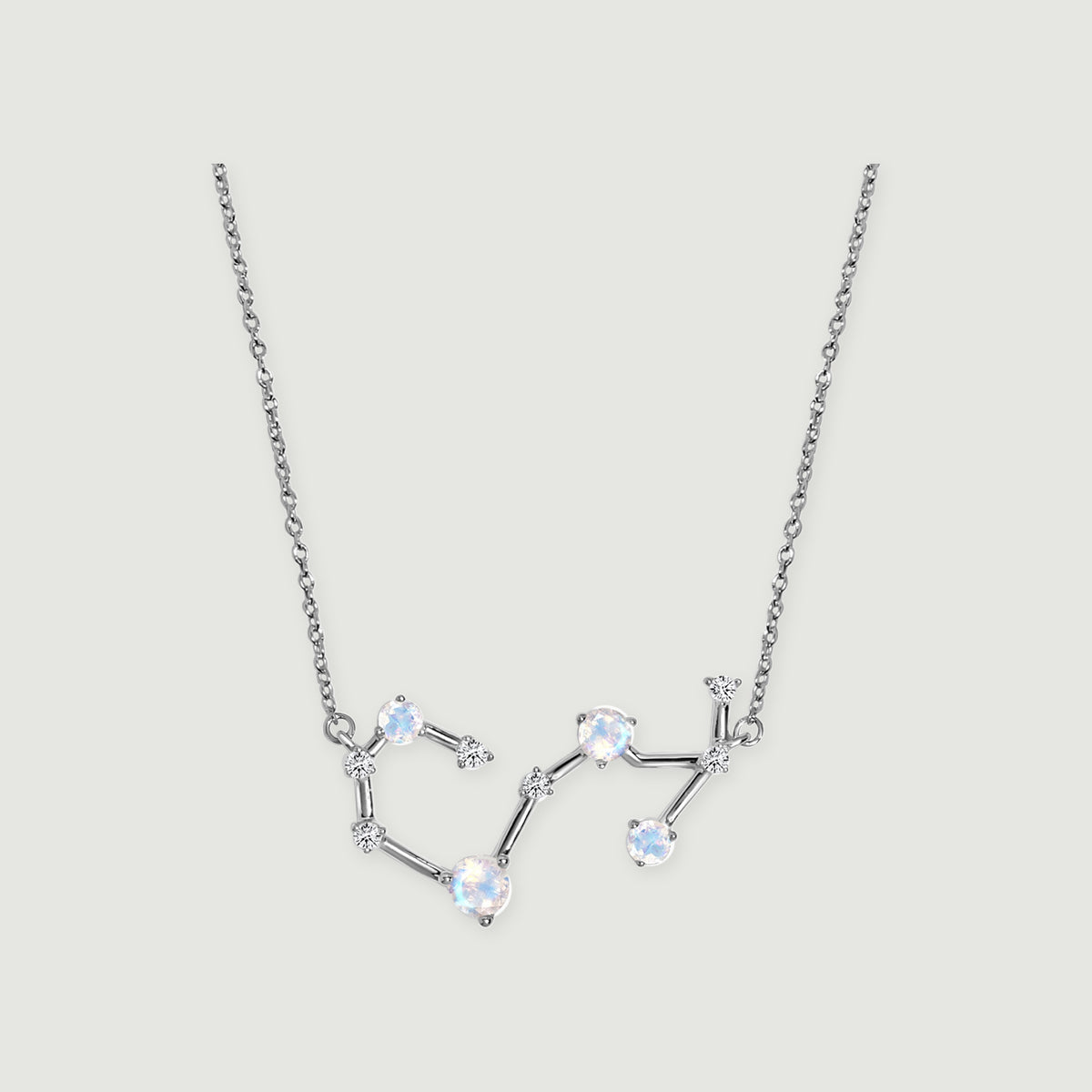 A silver necklace with round iridescent stones and small clear accents rests on a light gray background.
