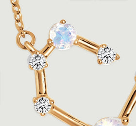 The left side of the gold pendant shows a pale round stone above two clear stones and polished connecting bars.