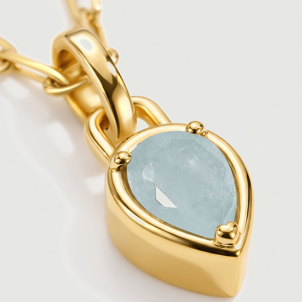 The pale blue aquamarine, rounded gold-colored prongs, and curved pendant bail fill this close view.