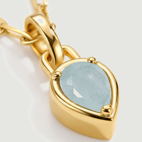 The pale blue aquamarine, rounded gold-colored prongs, and curved pendant bail fill this close view.