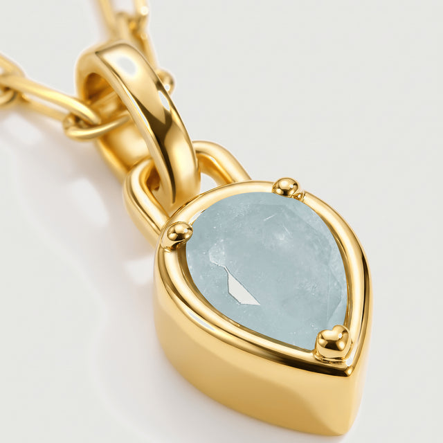 The pale blue aquamarine, rounded gold-colored prongs, and curved pendant bail fill this close view.
